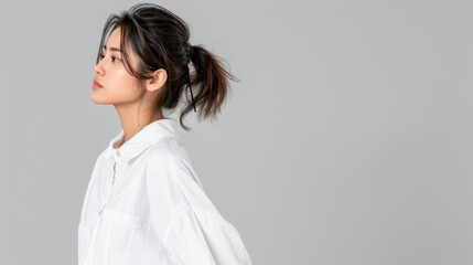 A stunning young Asian woman poses gracefully against a gray backdrop, showcasing her natural beauty and elegance.