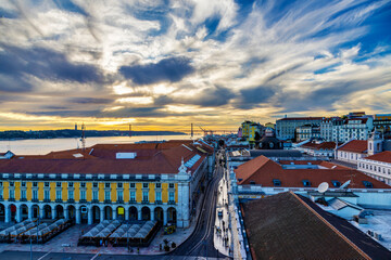 Sunset view atop Rua Augusta Arch overlooking Commerce Square and Rua do Arsenal Street toward Belem in Lisbon, Portugal, with April 25 Bridge in background across Tagus River