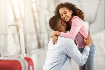 Meeting In Airport Concept. Little black girl embracing her happy father after arrival in airport, returning back home from vacation journey voyage, back view of man hugging daughter. Homecoming