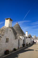 Alberobello, Italy. People walk down a Alberobello street, white washed, cone shaped roofs and flowers