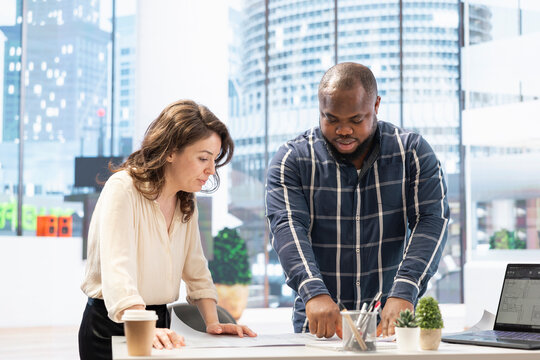 Realtor helping client to choose an office space in high class modern building, entrepreneur planning a relocation. People studying the architectural blueprints to present the property potential.