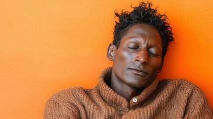Obraz premium A man with curly hair sits quietly against a vibrant orange wall. He appears serene and relaxed, enjoying a moment of peace in a cozy sweater