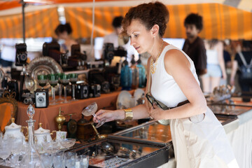 Interested woman chooses interesting antique items at a traditional flea market - crystal jam bowl