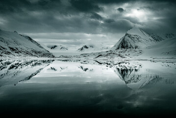 Svalbard, Norway. Black and white reflection of mountain, sky and clouds.