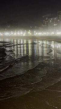 A vertical video of a nighttime beach view in Gijon, Spain.