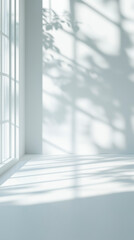 Obraz premium Bright minimalist interior with sunlight coming through a window and casting soft shadows of leaves on white walls and surfaces.