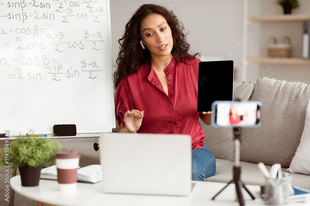Aufkleber Lady math teacher making video conference chat with students using laptop and cellphone on tripod, holding and showing tablet with empty screen with copy space for mockup, explaining