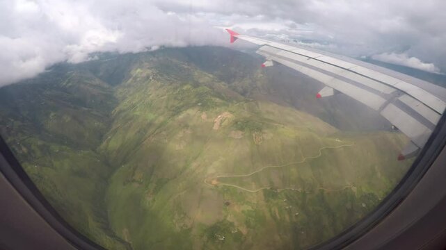 Looking through the window of a plane flying over the Andes. A road leads up the mountain range as we fly by above