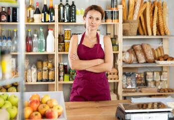 Adult female seller posing standing at counter in grocery store