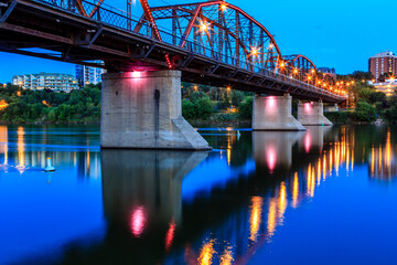 A bridge spans a river at night, with lights illuminating the structure