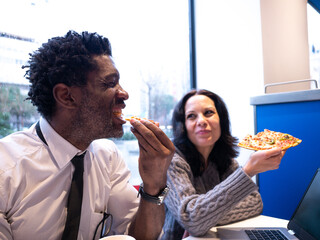 Two colleagues sharing pizza in a casual setting during a lunch break, promoting teamwork, relaxation, and office camaraderie.