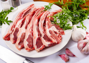Raw lamb chops on plate with garlic and herb, over white background.