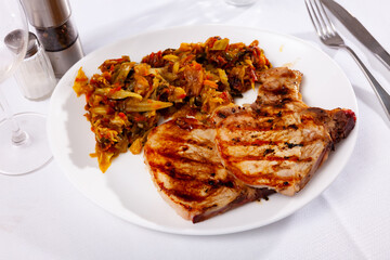 Portion of pork meat with stewed cabbage served on plate.