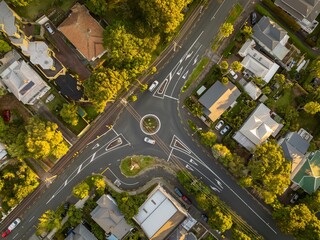 High-angle view of a residential neighborhood intersection with a traffic circle. Cars navigate the...