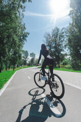 Obraz premium Rear view of Caucasian woman riding bike in park. Vertical photo. 