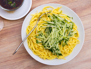Boiled thin noodles are cooked for lunch. Dish is served with slices of fresh cucumber and minced meat.