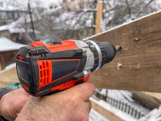 A hand with a screwdriver drills a wooden beam. Drill bit details and wood shavings are visible up...