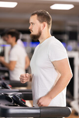 Obraz premium Man works out on a treadmill in a gym. Client of a fitness club performs a cardio warm-up