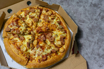Freshly baked American pan pizza with a lot of cheese, chicken sausage, thin and crispy kebab meat on a board, take-away dish