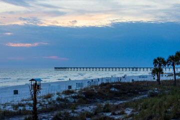 Fototapeta premium a beautiful sunrise over the Atlantic ocean with Panama City Beach City Pier, people walking, palm trees and waves at Panama City Beach Florida USA