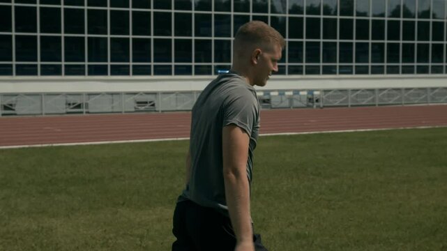 Medium rear side shot of male javelin thrower with acheiria disability, missing hand, practicing at outdoor stadium for competition, throwing spear at distance and watching it fly