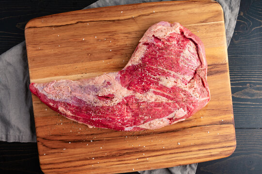Raw TRi-Tip Sprinkled with Kosher Salt and Black Pepper: Uncooked beef tritip on wooden cutting board seasoned with coarse salt and ground pepper