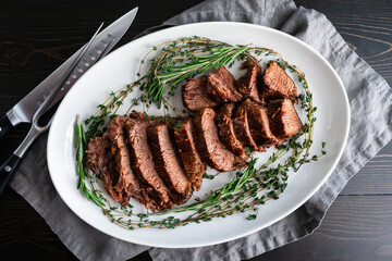 Sliced Tri-Tip Roast Beef on a Large Platter: Slices of roast beef surrounded with sprigs of thyme and rosemary on a ceramic plate
