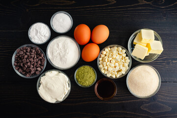 Matcha Cheesecake Brownies Ingredients: Green tea powder, dark chocolate, white chocolate, cream cheese, and more on a dark wooden table