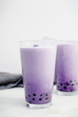 Two Glasses of Purple Sweet Potato Bubble Tea: Ube boba with ice cubes and clear silicone straws on a white background