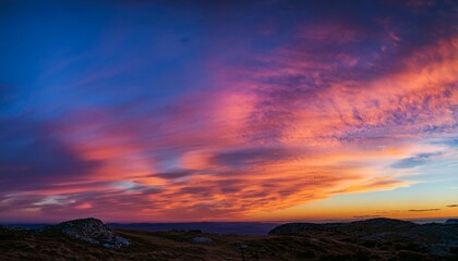 Fototapeta premium Vibrant sunset colors paint the sky over a hilly landscape.