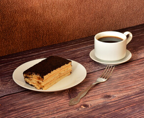 Plate with Italian dessert Tiramisu, cup of black coffee on a saucer and fork on a dark wooden table.