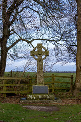 A historic Celtic cross monument set amidst the tranquil countryside near Stonehenge, UK. Framed by bare tree branches, this ancient structure stands as a symbol