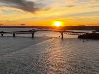 Obraz premium Golden sunset over the Auckland Harbour Bridge. Boats navigate the calm waters. Beautiful scenery. Auckland Harbour Bridge, Auckland, New Zealand