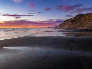 Dramatic sunset over a black sand beach. Coastal cliffs meet the ocean at twilight. Peaceful,...