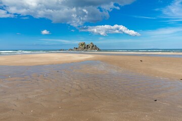 Tranquil beach scene with low tide, rocky outcrop, and a lone bird. Coastal beauty on a sunny day. Opoutere, Whangamata, Coromandel Peninsula, New Zealand