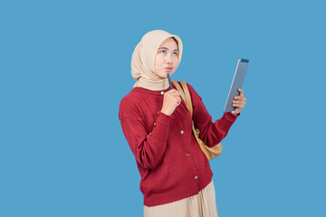 A woman wearing a red sweater and a tan head scarf is holding a pen tablet and looking up. She is...