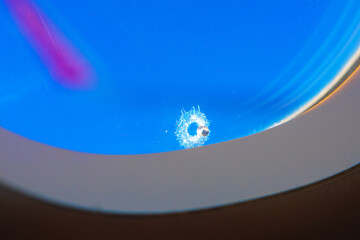 Little hole in airplane window against vivid blue sky. Highlighting the fragility and resilience of...