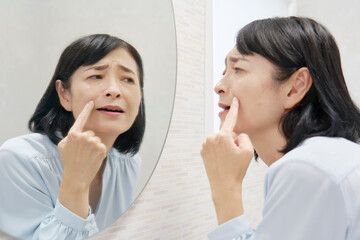 鏡で顔を見て悩む50代の女性