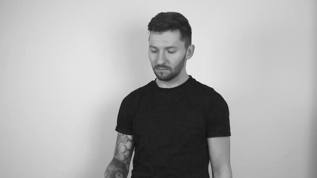 Grayscale footage of a tattooed short haired man spinning a bitcoin coin in slow motion by throwing it into the air and catching it. after catching he shows the shiny coin directly to the camera.