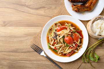 Spicy papaya salad (Som Tum) eating with sticky rice and grilled chicken wing on wooden table, Local Thai food