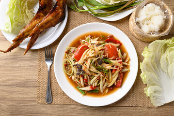 Spicy papaya salad (Som Tum) eating with sticky rice and grilled chicken wing on wooden table, Local Thai food