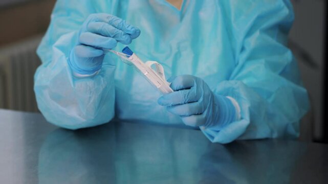 A doctor in a blue protective suit opens the sterile packaging of a swab for analysis. Opening the package with a medical swab. Modern medical laboratory.