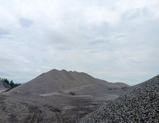 A large mound of gravel and sand shaped like a mountain under a cloudy sky at a natural mining site.