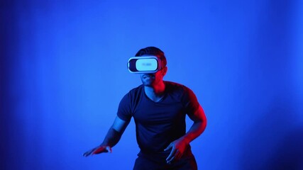 Caucasian man playing basketball while wearing VR headset at blue background. Skilled athlete holding basketball while entering and access metaverse by using virtual reality technology. Apparatus. - Powered by Adobe