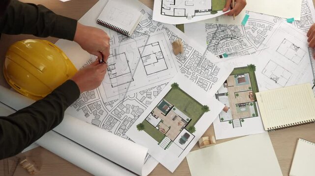 Architect and safety engineer discussion about building construction use blueprint on table with architectural document, measurement tool and wooden block scatter around at modern office. Delineation.