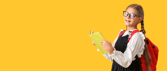 Cute schoolgirl with book and backpack on yellow background