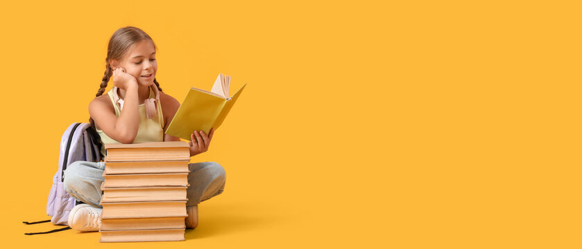 Cute schoolgirl reading book with headphones and backpack sitting on yellow background