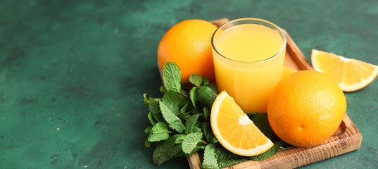 Glass of fresh orange juice and mint on green background with space for text