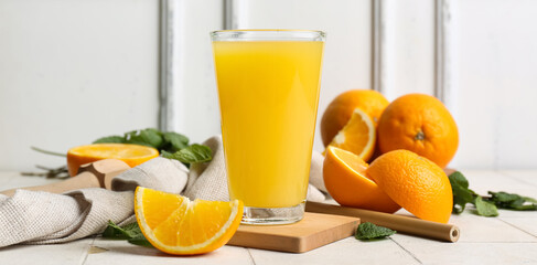 Glass of tasty juice with oranges and mint leaves on white tile table