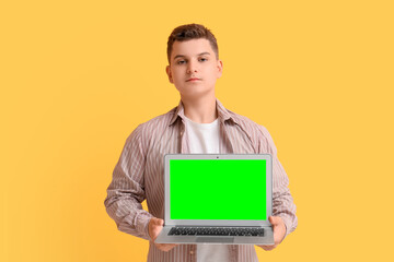 Teenage boy holding laptop with blank screen on yellow background